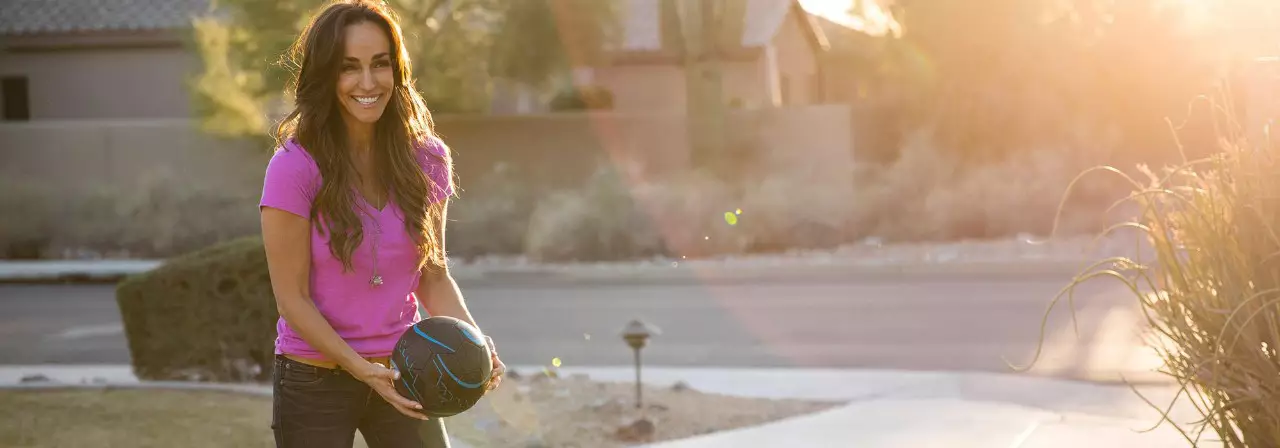 Woman holding a soccer ball and smiling standing in a neighborhood.