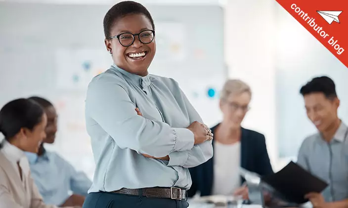 Smiling employee in the forefront and blurred out co-workers working in the background happily