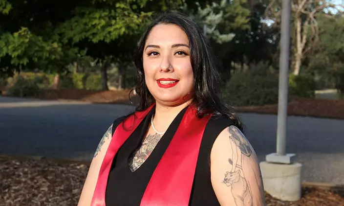 Alumni Andrea Romo smiling and wearing graduation regalia