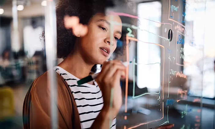 A female doctoral graduate writing on a dry erase board, participating in a postdoc research program.