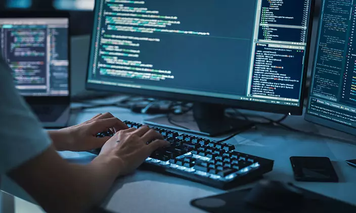 Hands on keyboard centered among three computer monitors