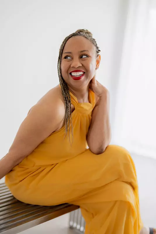 Freda Richards laughing while seated in a yellow dress, glowing with joy.
