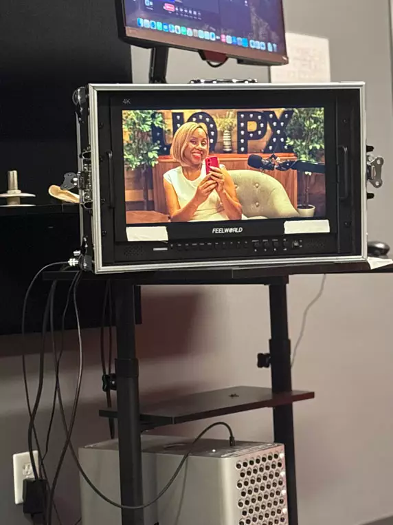 A monitor showing Freda Richards smiling and holding her phone during a recording session in the Degrees of Success podcast studio.