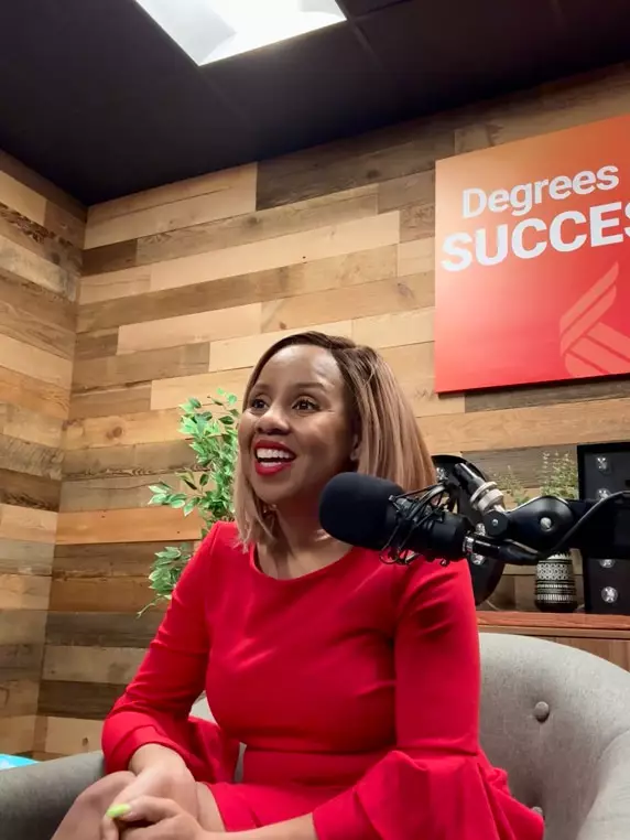 Freda Richards sitting in front of a microphone in the Degrees of Success studio, smiling in a red dress with a wood-panel background and podcast signage.