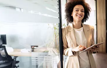 An auditor, carrying a notepad, enters the hallway at her place of business.