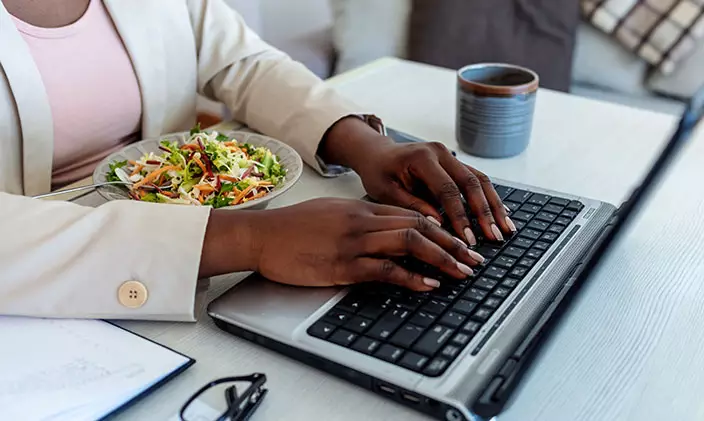 African american woman working on laptop and eating a salad