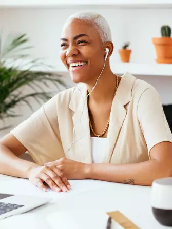 Business professional with earbuds smiles as she chats with colleague online