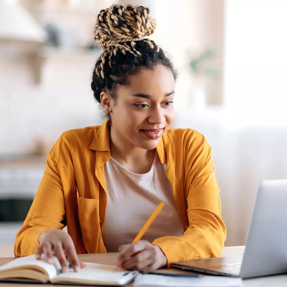 Happy student with laptop writes notes in her notebook about how to earn college credits for her job experience