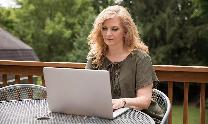 Student sits on her home's deck with a laptop to work on a paper