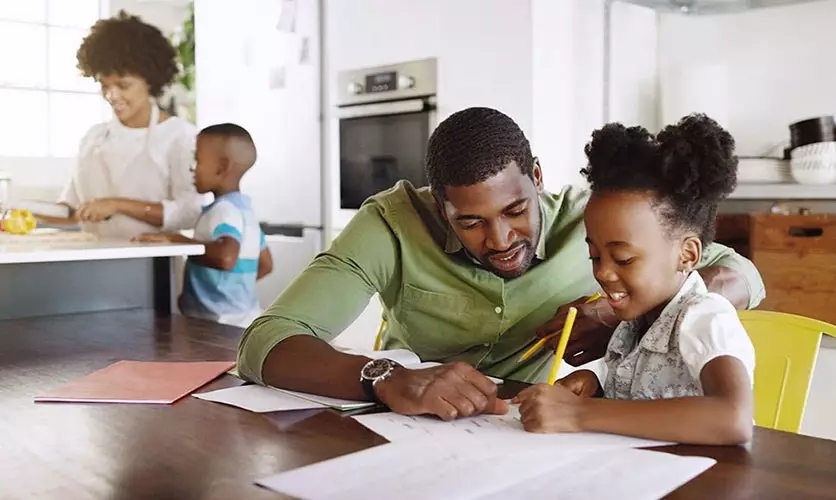 At the family's kitchen table a father helps his daughter with homework