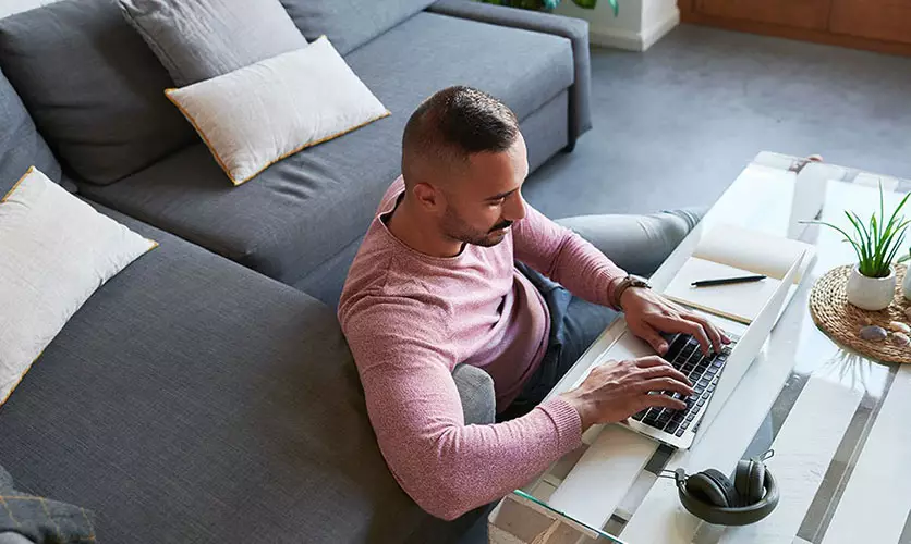 Student sitting on living room floor types on his laptop on coffee table