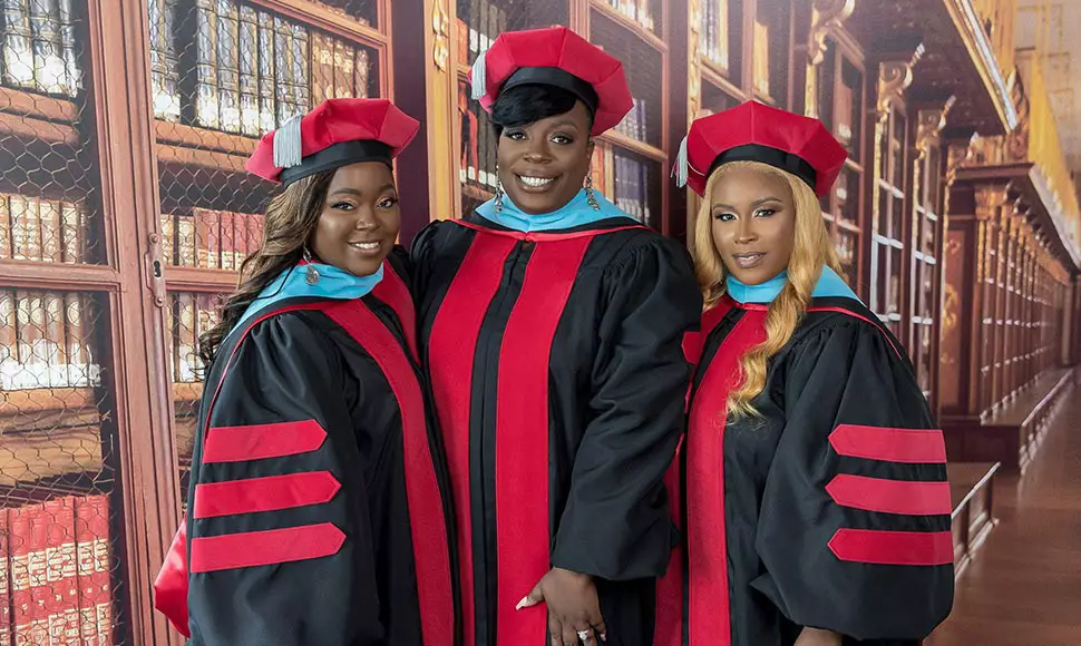 Three alumni and best friends stand in their doctoral regalia