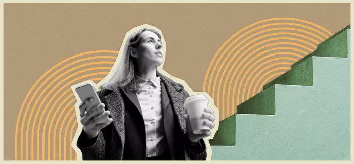 Businesswoman with phone and coffee looking up next to stairs.