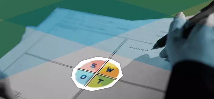 A hand holding a pen above a piece of paper used to map out a SWOT analysis that has SWOT written in a big circle in the middle