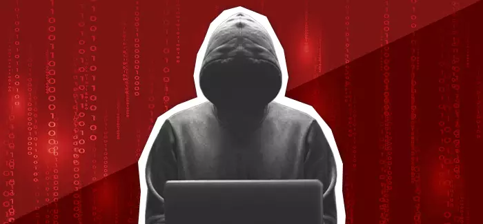 A hooded figure in front of a laptop computer infecting it with spyware, in front of a dark red background with computer code on it.