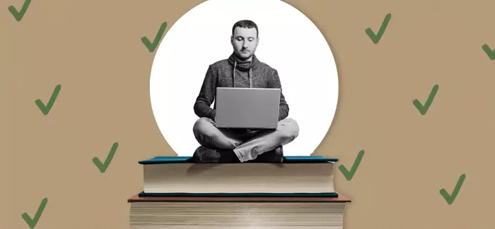 Man sitting on a stack of books, working on his laptop on his ace credits