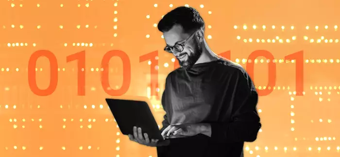 Male student using a laptop to hone his internet technology skills, standing in front of a wall of binary code