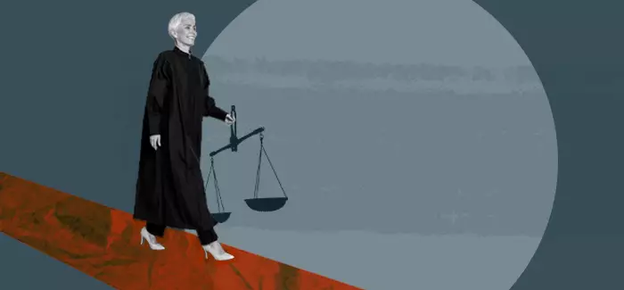 Woman in a judge's robe walking holding the scales of justice