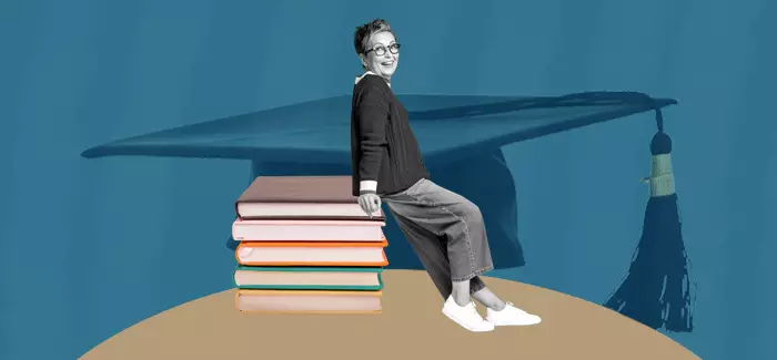 Woman who has just earned her Doctor of Education, leaning back on a stack of books with a graduation cap in the backgrouns
