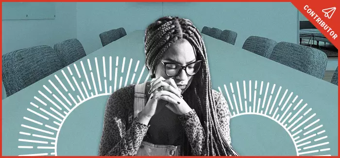 African american woman looking sad and gazing down with hands folded at conference desk.