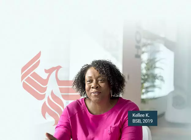 A photo of Kellee K., BSB, 2019, smiling at the camera and seated in a campus meeting room