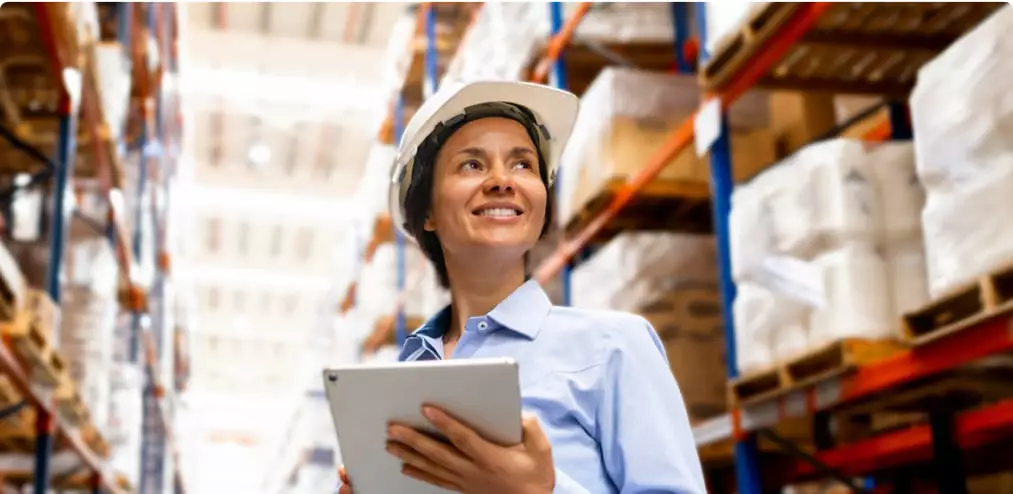 A confident woman in a hardhat in a warehouse setting, symbolizing skill development and career growth in a professional setting.