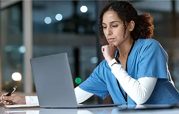 A charge nurse writes on notepad while looking at a laptop screen