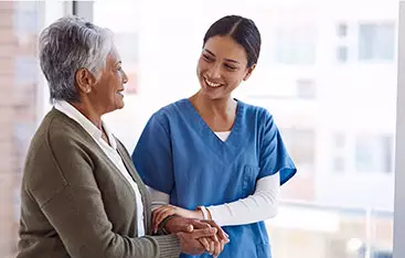 A charge nurse gives a patient a steadying arm as they walk and talk