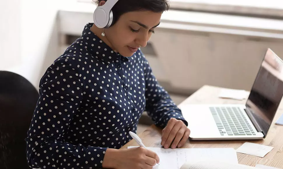 Employee taking notes and listening to music to represent employees benefit from tuition assistance