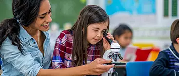 A teacher assists a young student in using a microscope