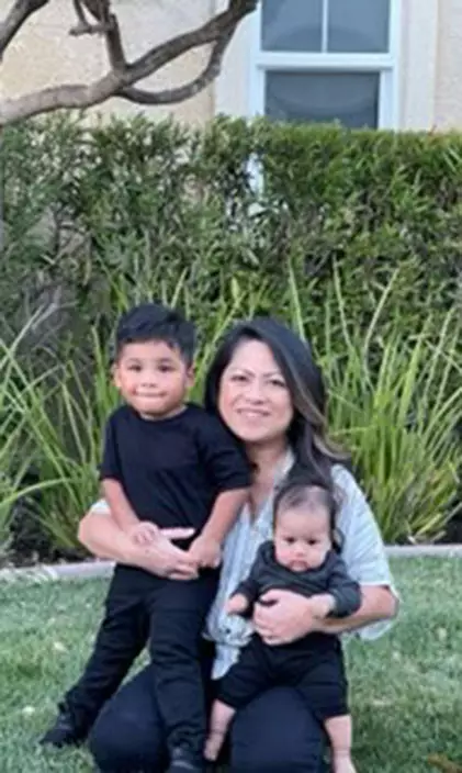 Emely holding two children smiling outside of house