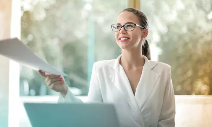 Woman at laptop handing paperwork off to someone else