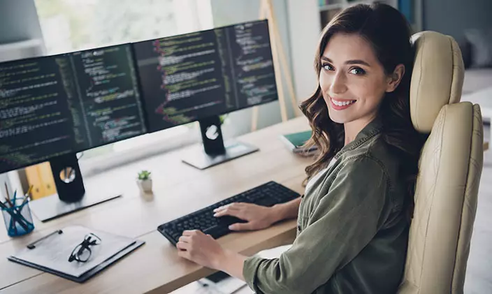 Friendly female programmer at her desk with two monitors