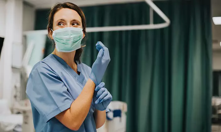 Female RN wearing a surgical mask putting on latex gloves