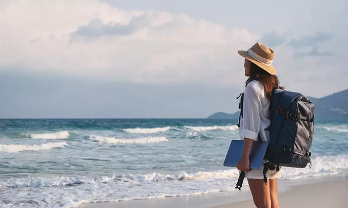 Female traveler holding laptop and looking out toward the ocean