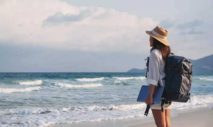 Female traveler holding a laptop while gazing at the ocean