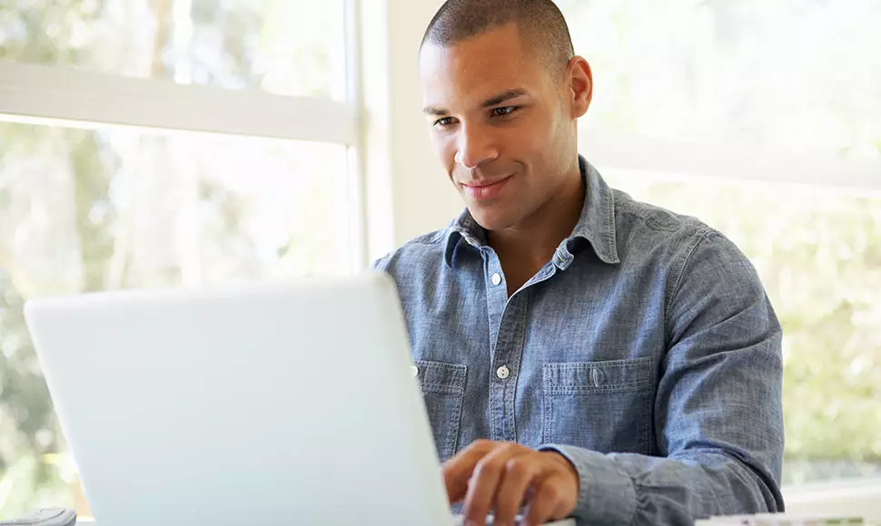 First-generation college student smiles faintly at his laptop