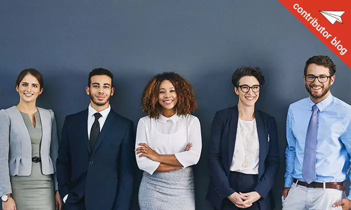 Group of smiling business people stand against a gray wall
