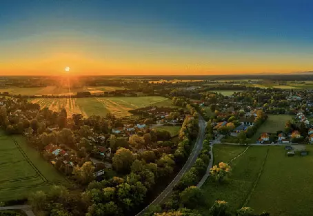 The sun sets over a rural setting with lush green fields surrounding a town