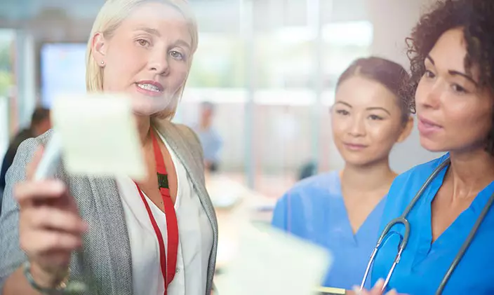 A woman in healthcare leadership showing a post-it note board to two nurses
