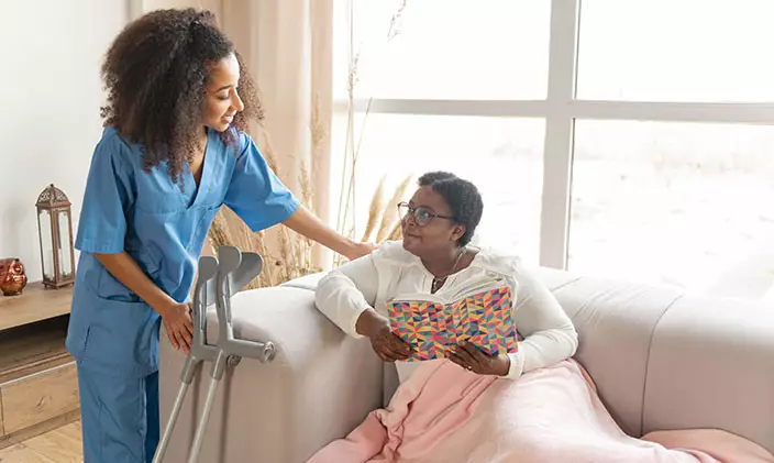 A home healthcare professional checking in on an elderly woman reading a book