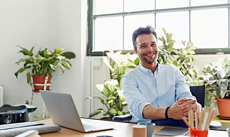 Smiling man sitting at home office with open laptop 