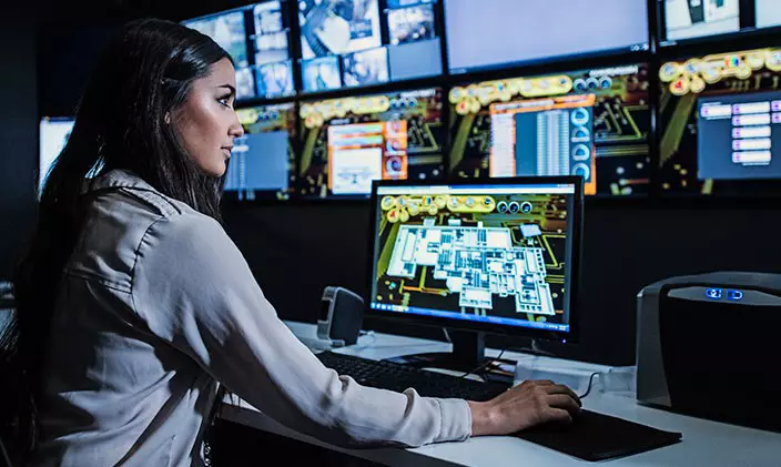 Female cybersecurity professional stares at a bank of computer monitors