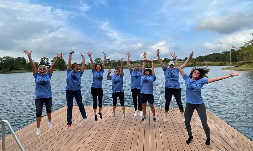 Female participants at Save A Warrior jump in triumph on a lake deck