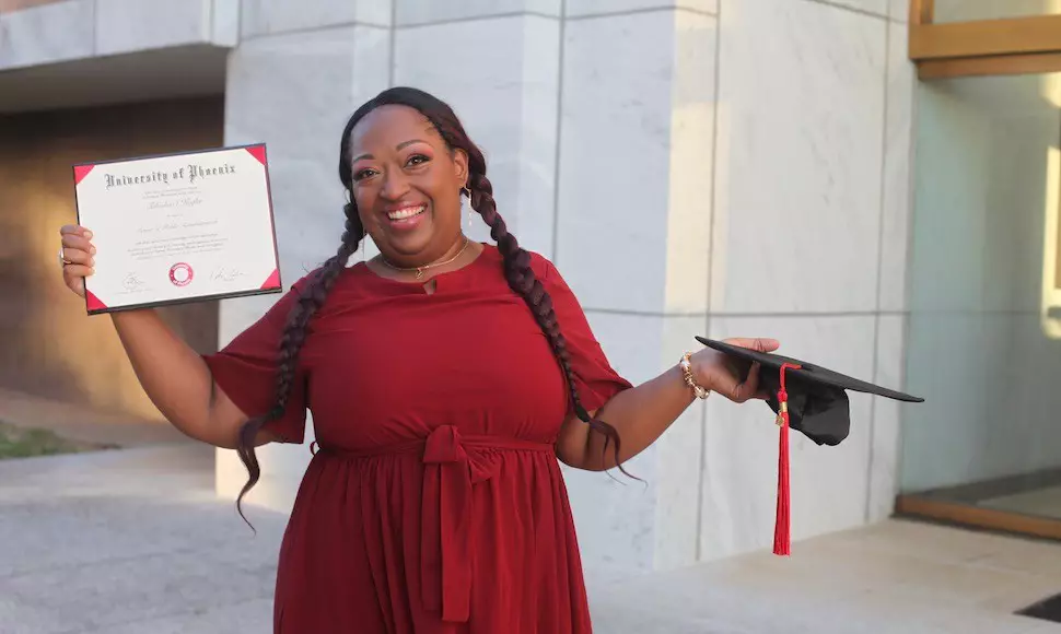 University of Phoenix alumni TaKisha Kegler holding her degree and graduation cap