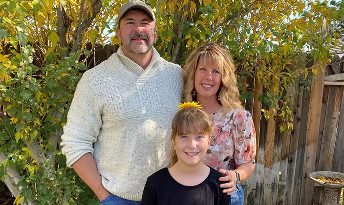 Laura Docter-Bennett smiles outside with her husband and daughter