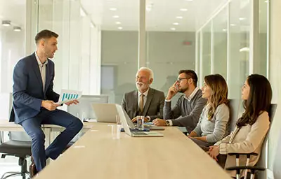 Colleagues, seated at a table, listen to a leader