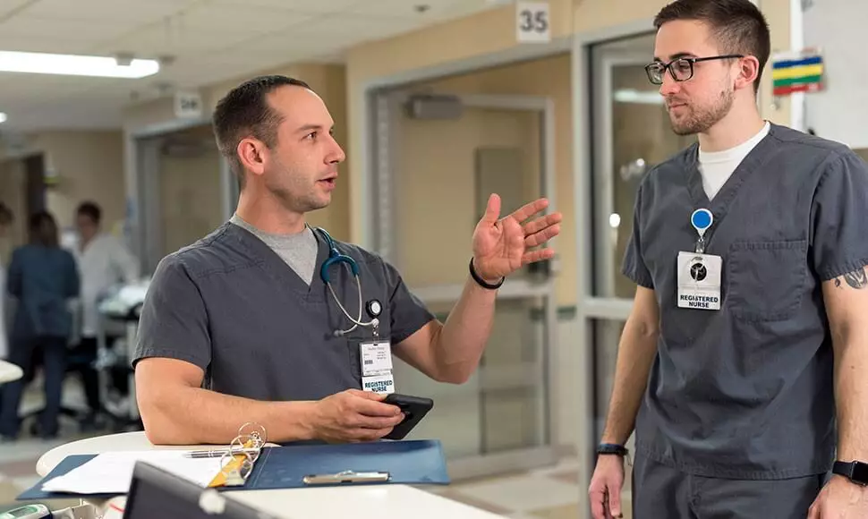 Two male nurses converse in a hospital setting