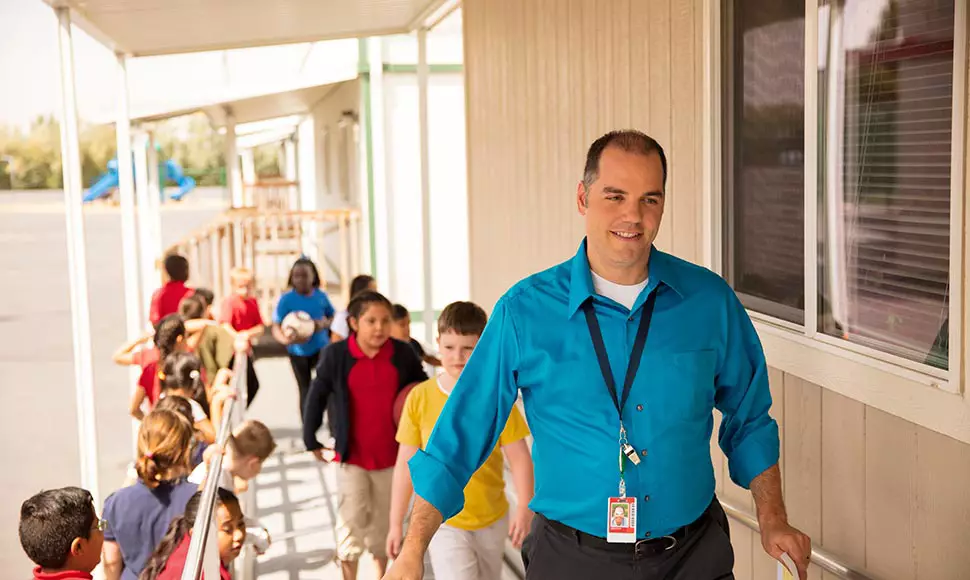 An elementary school teacher leads his young class back inside from recess.