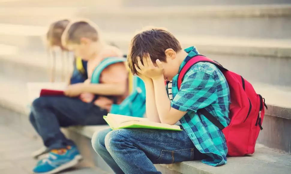 School boy holds his head in his hands while wearing a backpack